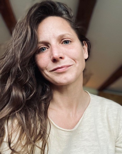 Sim, 43, sitzt entspannt in Alltagskleidung auf einem Stuhl und lacht, sie trägt den Brakini unsichtbar unter ihrem Outfit und wirkt gelöst.